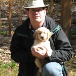 Man in hat holding a golden retriever puppy.