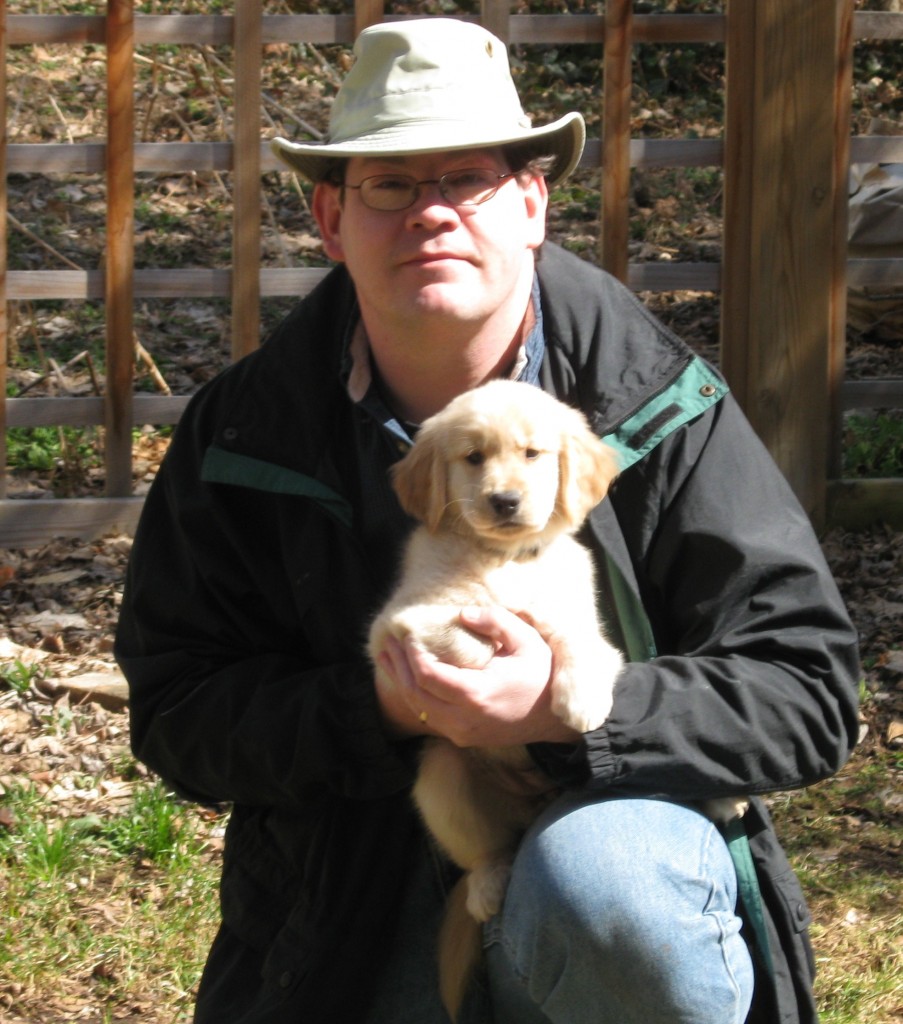Man in hat holding a golden retriever puppy.