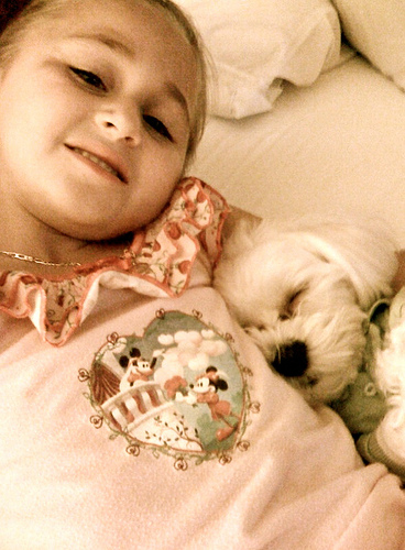 A little girl sleeps with her dog.