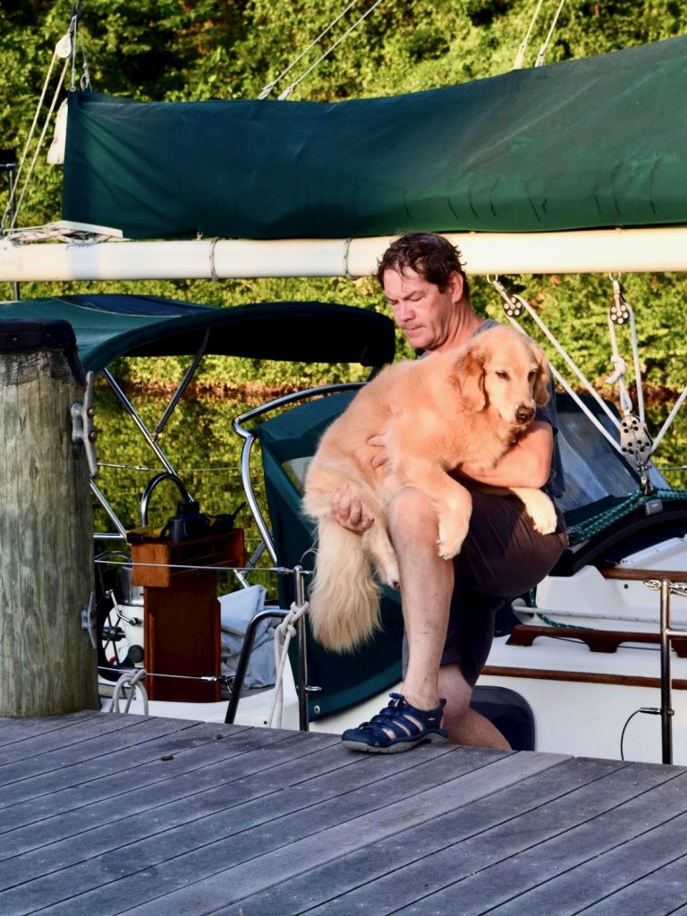 Man lifting golden retriever off sailboat onto dock.